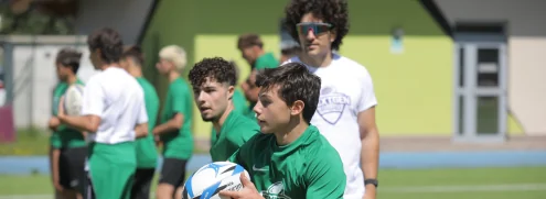 Young rugby player carrying the ball with teammates and coach at a summer camp